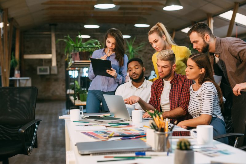 Agency coworkers discussing new project on laptop, working in modern office, free space